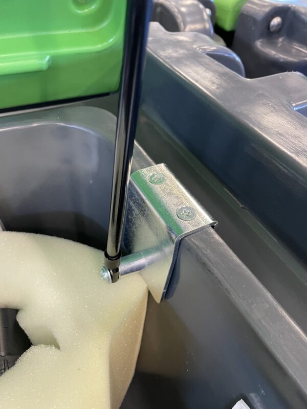 Närbild av ett metallfäste med två skruvar som fäster en Gasdämpare till TruckMaster-serien på en grå plastyta, bredvid ljusgult skum; grön plast syns upptill.