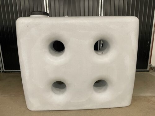 ÄlvestadTanken Vattentank SQVB 2000L, en stor rektangulär vit plasttank med fyra cirkelformade fördjupningar i ett fyrkantigt mönster, står på ett betonggolv mot en svart räfflad bakgrund.