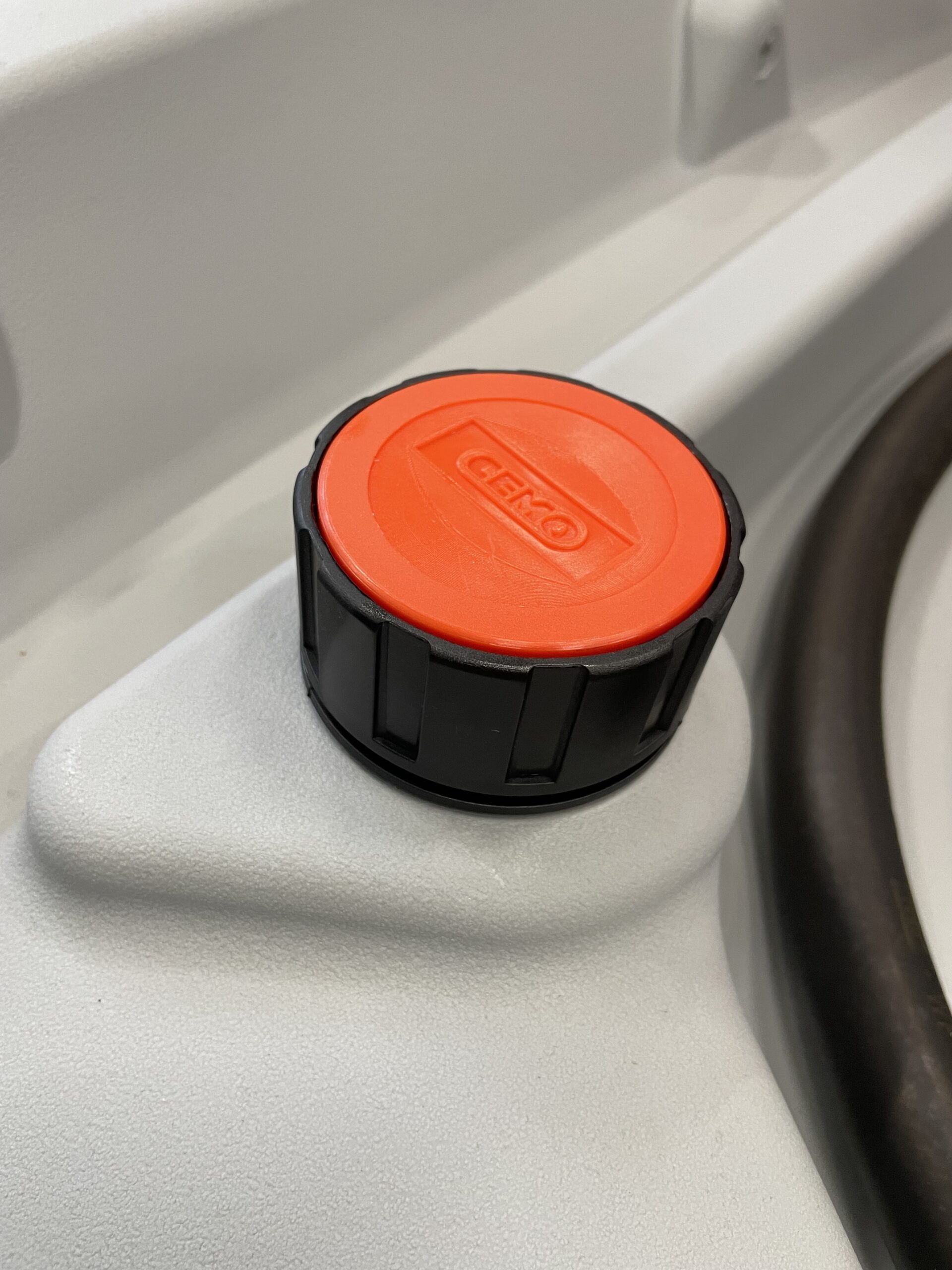Närbild av ett svart och orange Tanklock Cemo DT-Mobil Easy 2" Endast Lock-lock märkt GEKO på en vit gjuten yta, möjligen en tank eller behållare, med en svart slang till höger.