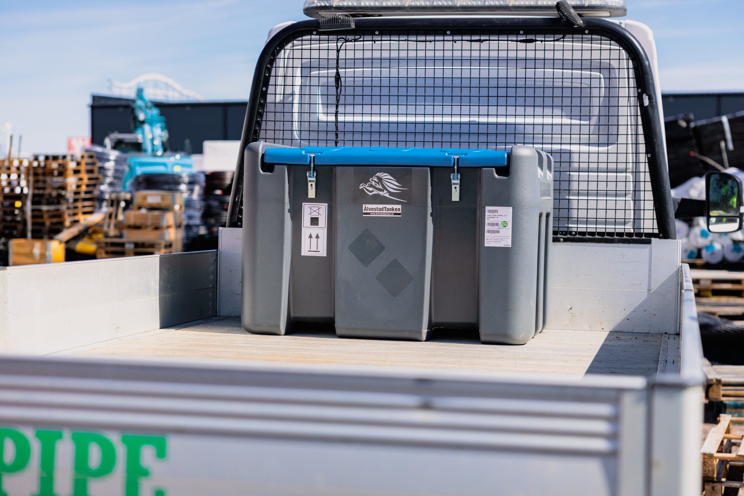 En TruckMaster KOMBI 400/40 Diesel/AdBlue förvaringscontainer med blå handtag är placerad på ett flak till en lastbil, parkerad på en industrigård med pallar och utrustning i bakgrunden.