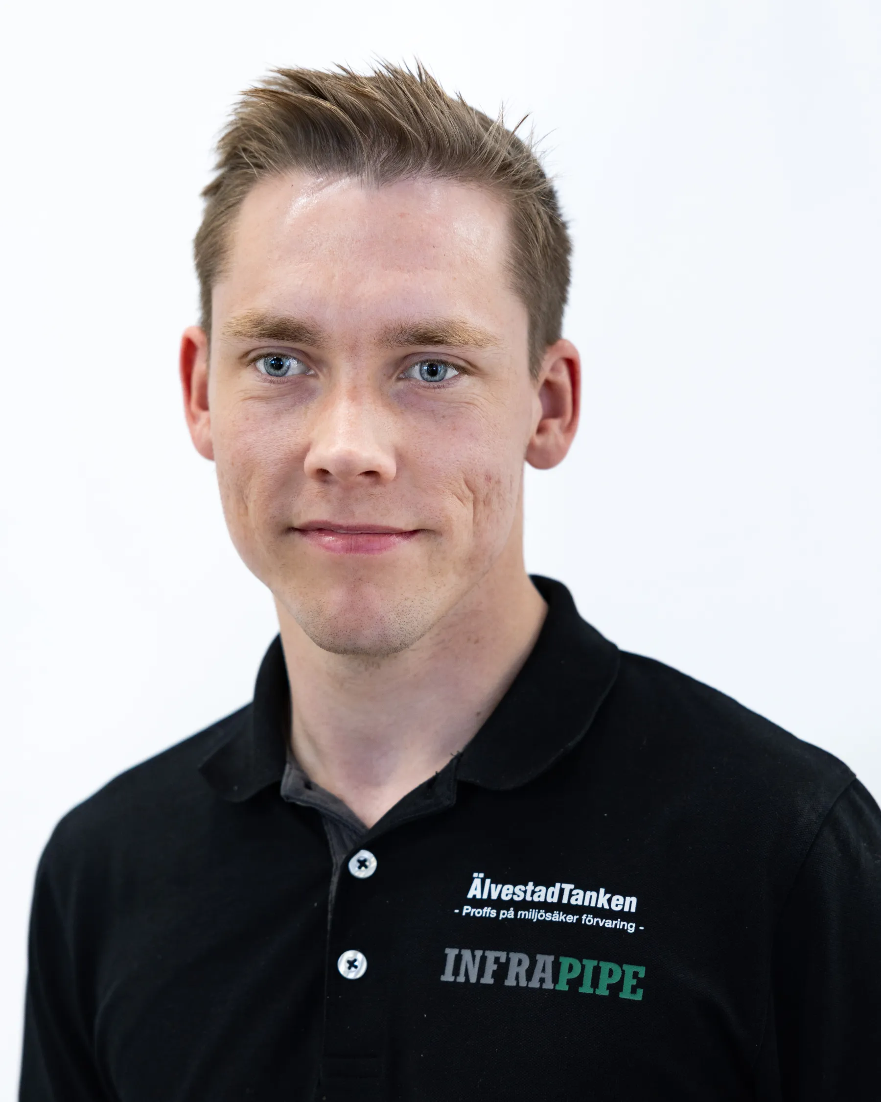 En ung man med kort ljusbrunt hår, klädd i en svart skjorta med krage och logotyperna ÄlvestadTanken och INFRAPIPE, står mot en vit bakgrund.