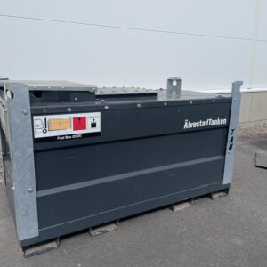 En ÅvestadTanken bränsletank i grå metall märkt "Uthyrning - Isolerad dricksvattentank 3500, 5000 & 9000 liter (kopia)" sitter på pallar utomhus vid en vit byggnad och svarta tunnor, med synlig varningsskylt och identifieringsdetaljer.