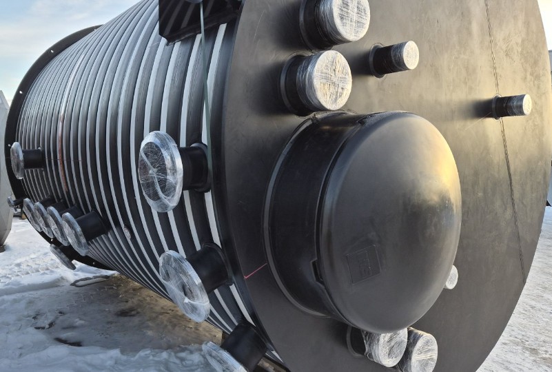 En stor cylindrisk industritank med flera röranslutningar med lock ligger horisontellt på en snöig yta. Tanken har svarta och silverfärgade räfflade sidor och plastöverdrag på rörändarna.