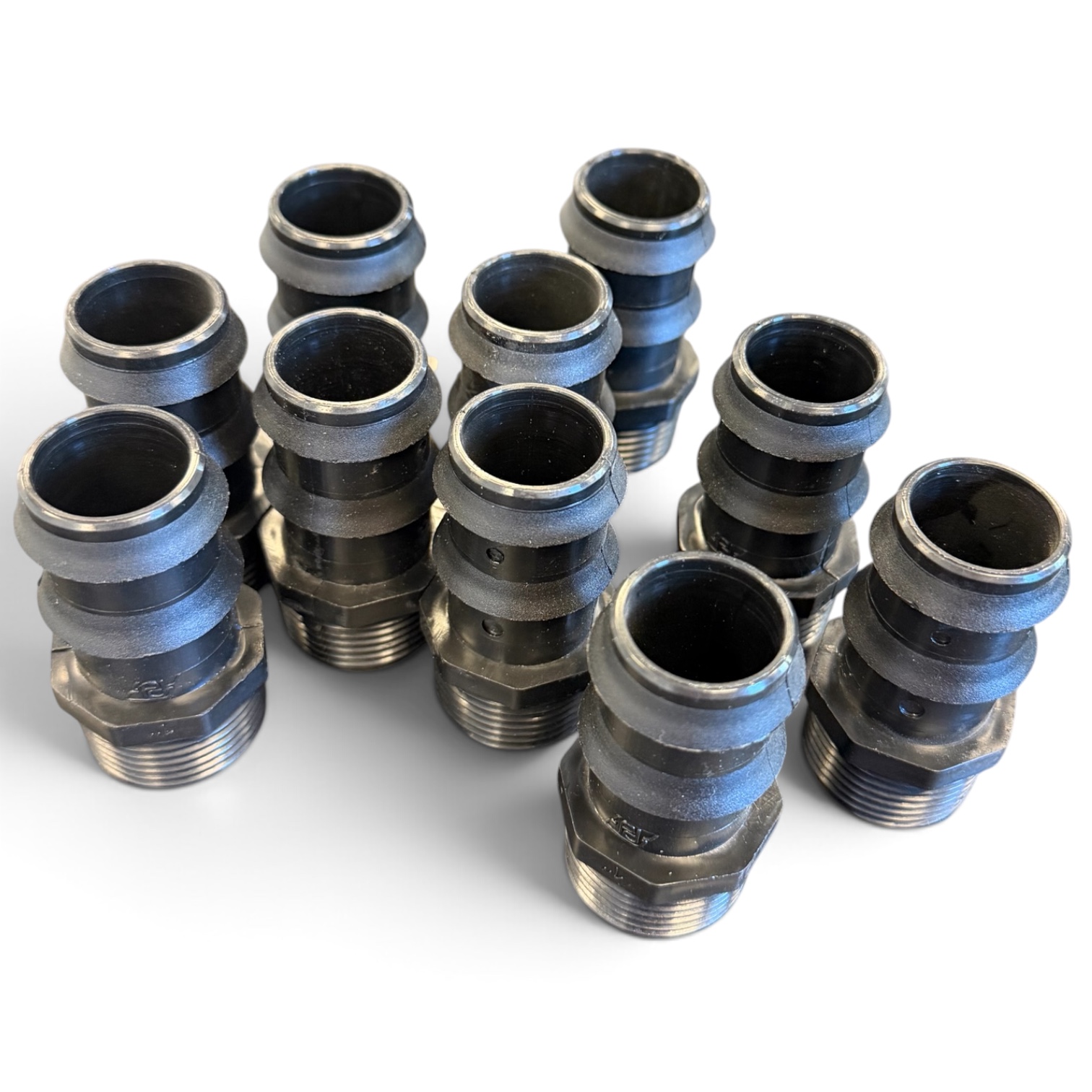 Tio Slangsockel-kopplingar (25 mm x 1”) (10-pack) i svart metall är placerade upprätt på en vit yta i tre löst ordnade rader; varje koppling har räfflade partier och gängade ändar.