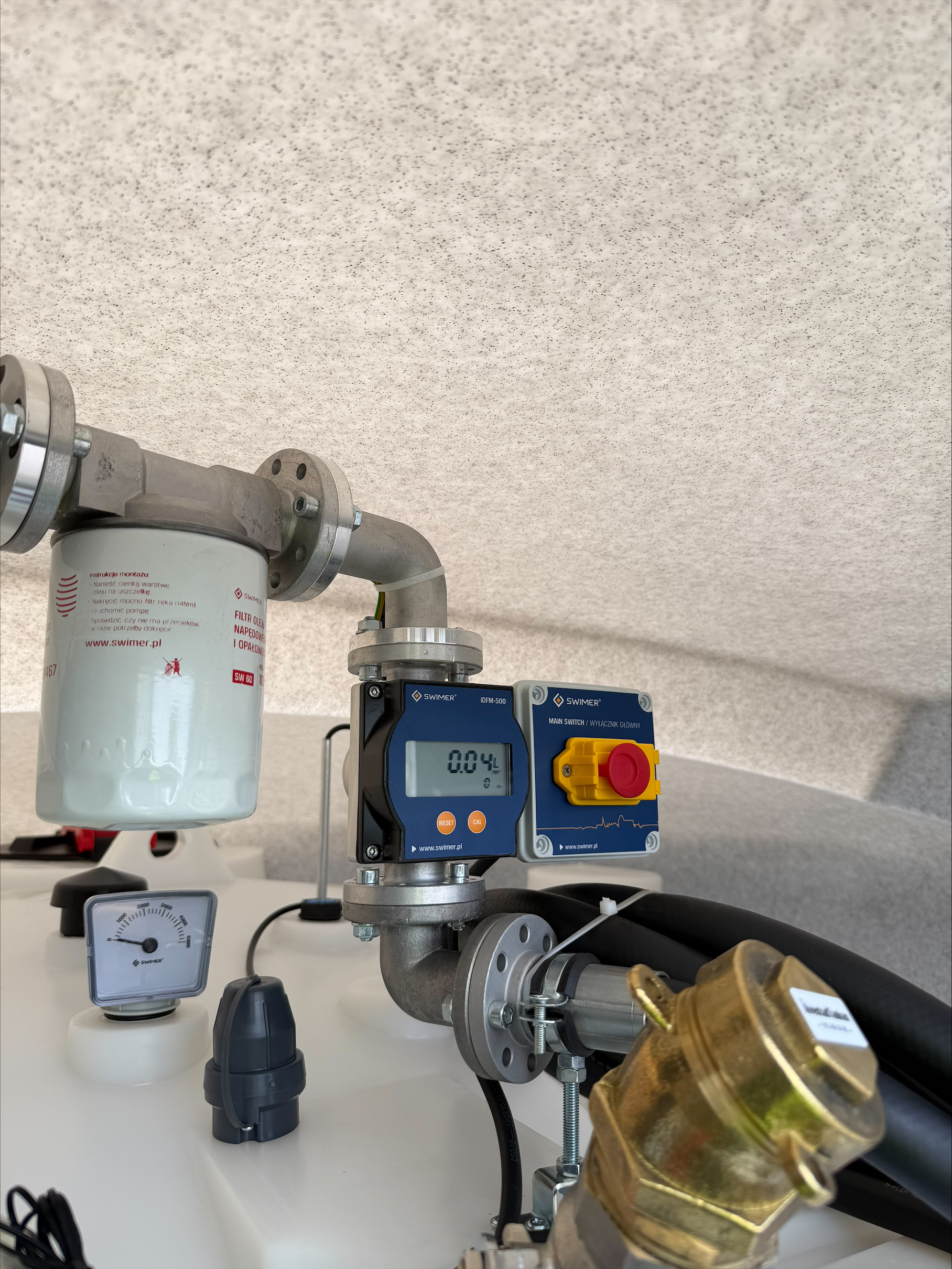 Närbild av Dieseltank Eco Line Basic 5000 liter med industriella mätare, ett filter, en digital display som visar 0,04 och en stor gul och röd nödstoppsknapp. Rör och kablar är anslutna till enheten.